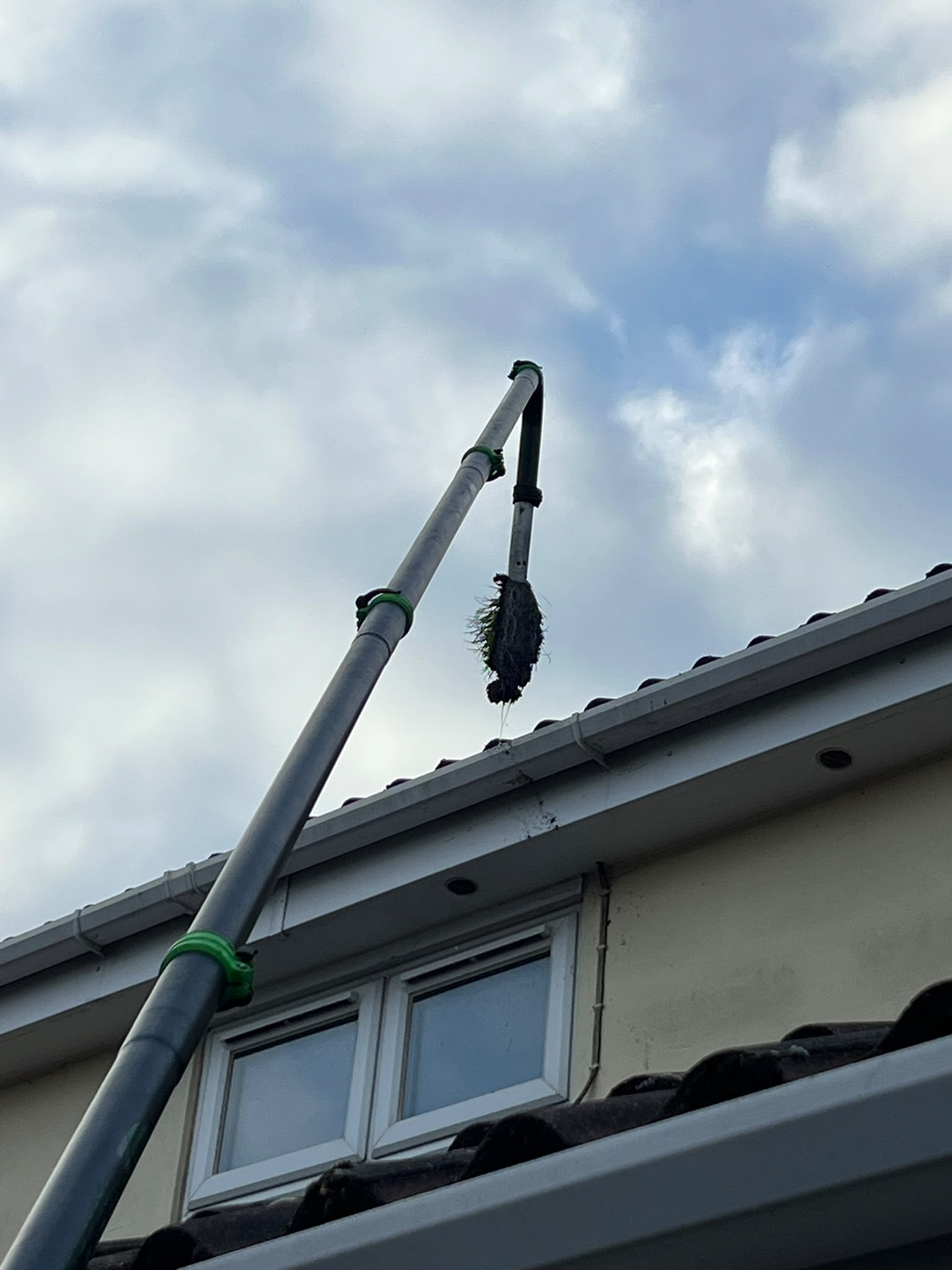 A clump of gutter debris lifted by a vacuum nozzle beside the roofline
