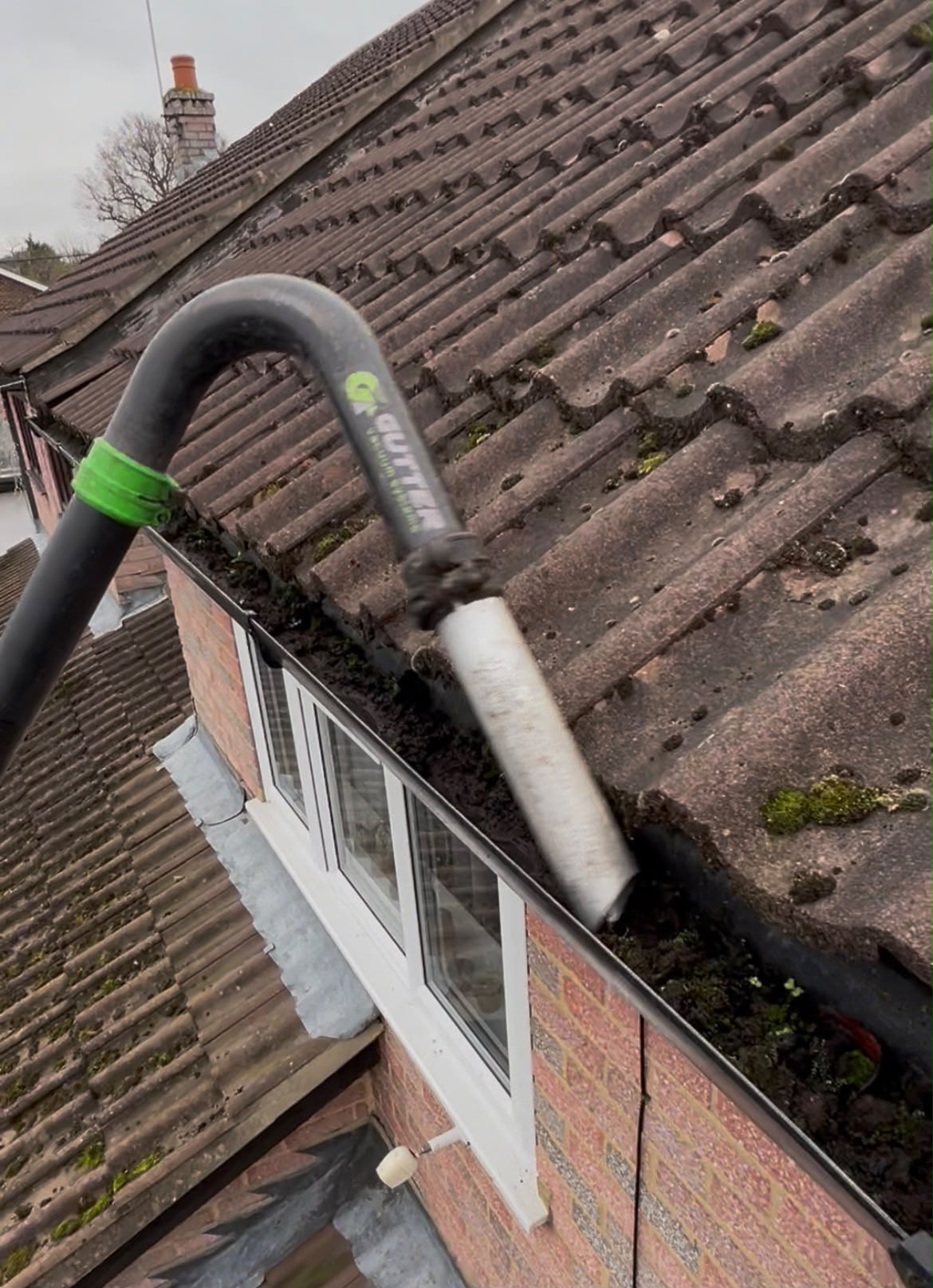 Gutter vacuum nozzle working along a gutter containing moss and debris